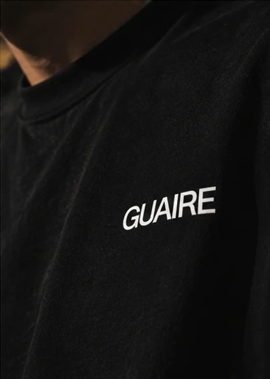 Close-up of the white GUAIRE chest print on black cotton.